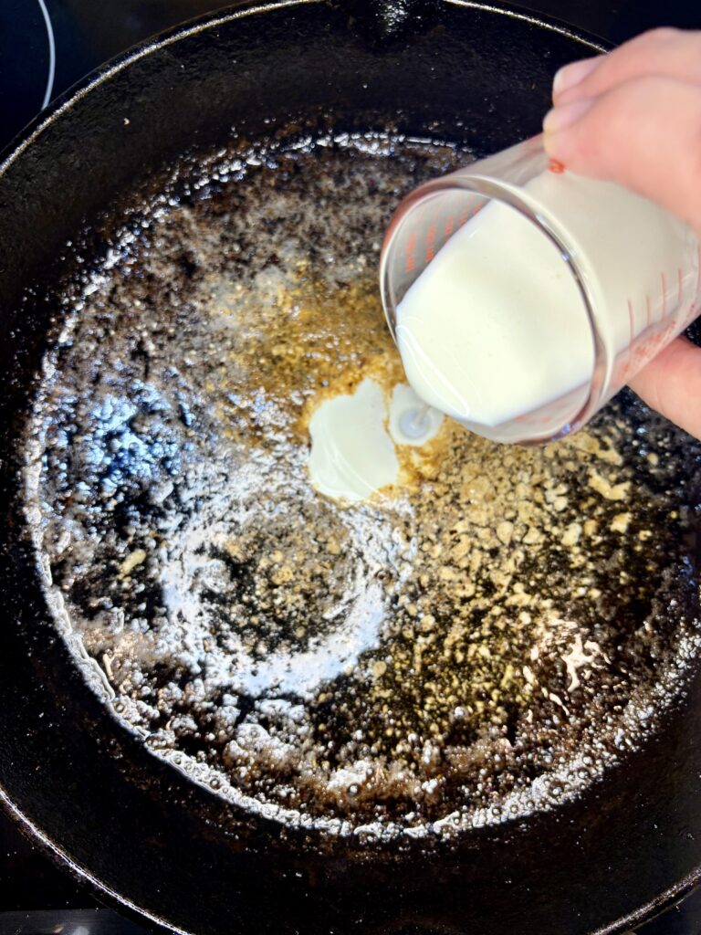 heavy cream being poured into skillet with pan juice