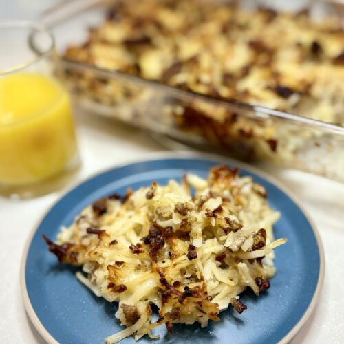 cooked sausage potato casserole on a plate next to a glass of orange juice