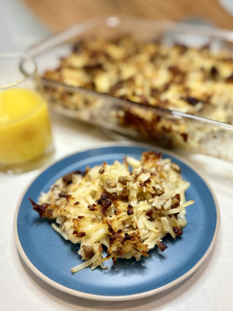 cooked sausage potato casserole on a plate next to a glass of orange juice