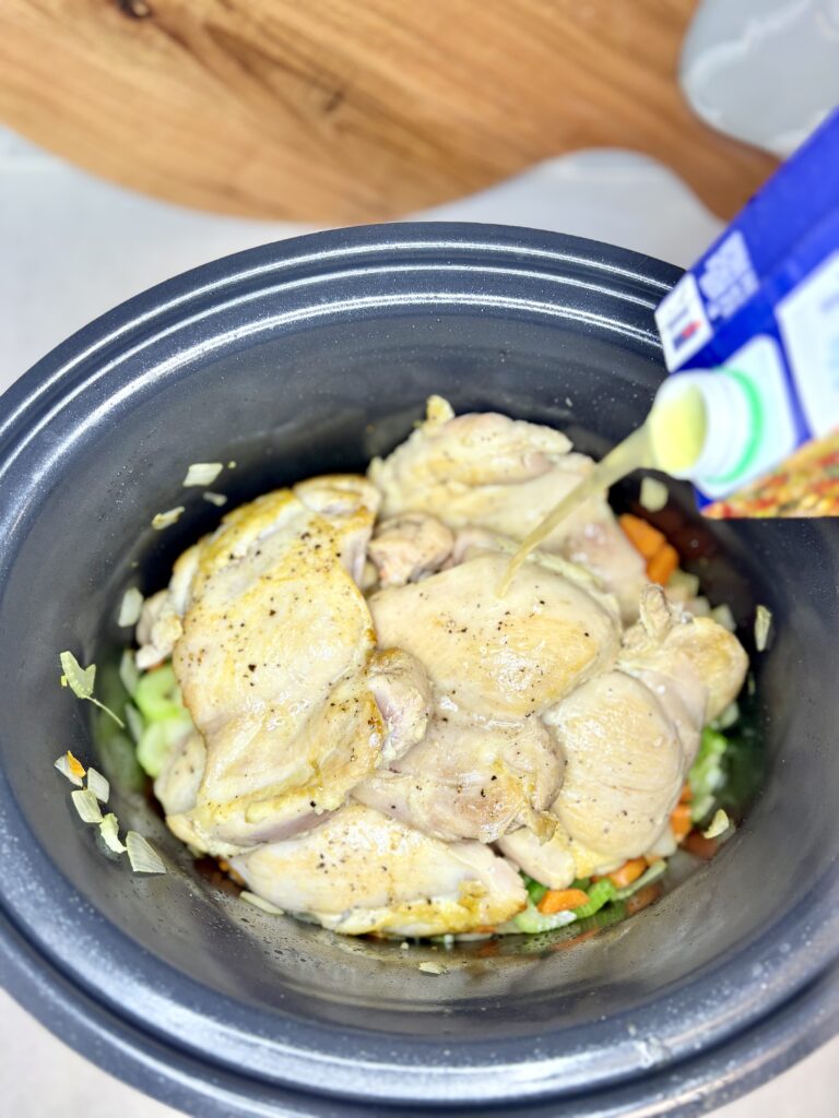 chicken and vegetables in a slow cooker with broth being poured over them