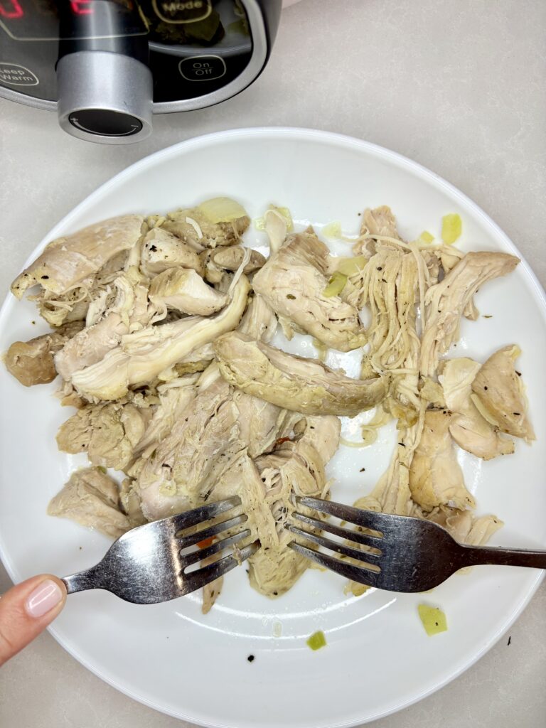 cooked chicken thighs being shredded with two forks