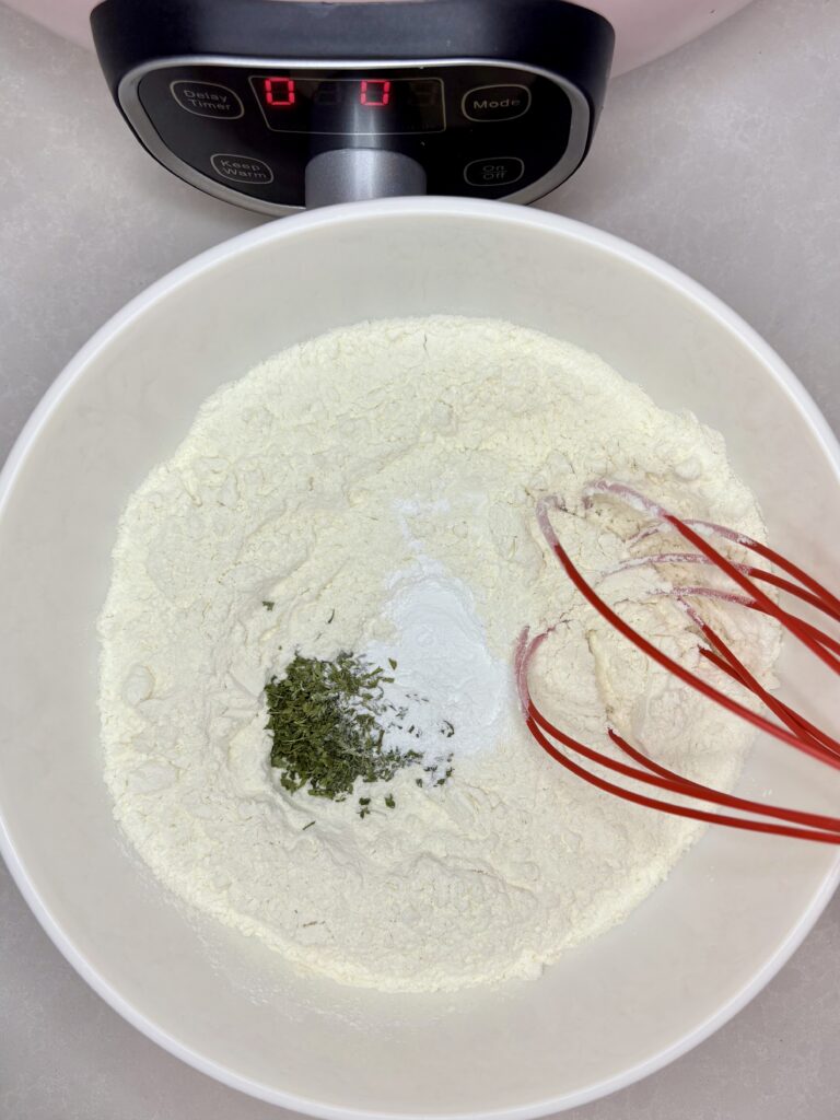 flour, baking powder, salt, pepper and parsley being whisked together in a bowl