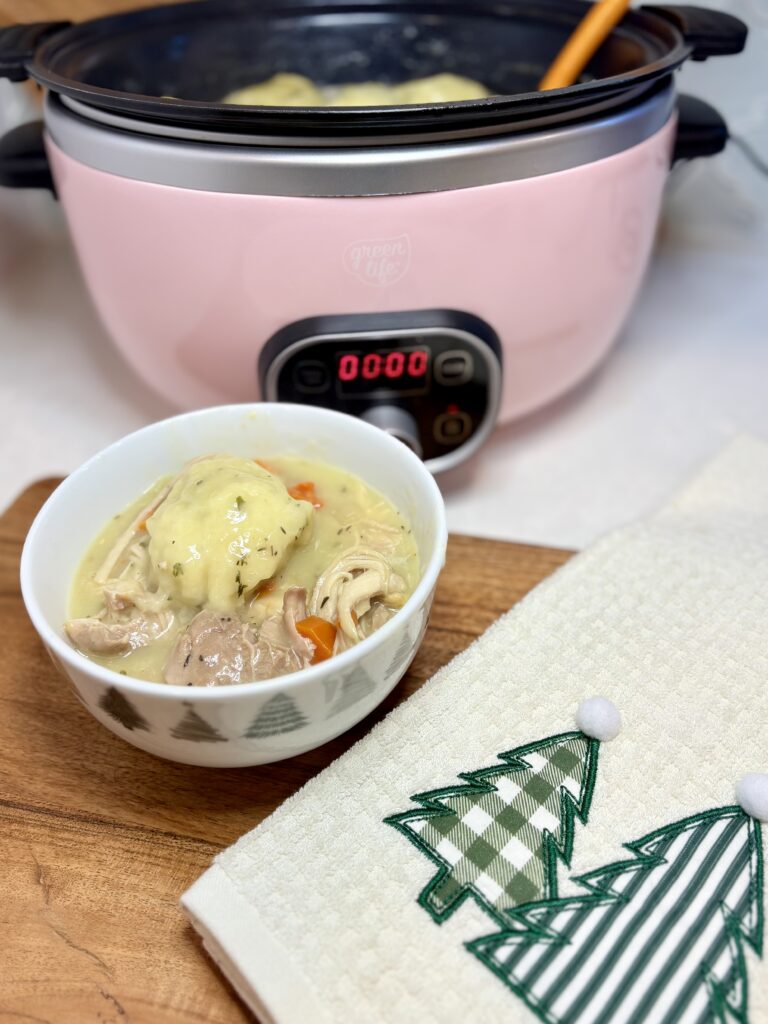 a bowl of slow cooker chicken and dumplings next to a slow cooker on a counter