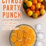 Bright citrus punch with sliced oranges in a large glass bowl, surrounded by fresh lemons, limes, and oranges in a wooden bowl, perfect for summer parties and gatherings.