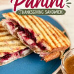 Leftover turkey panini with cranberry sauce on a blue plate, grilled to golden brown, served with a side of gravy.