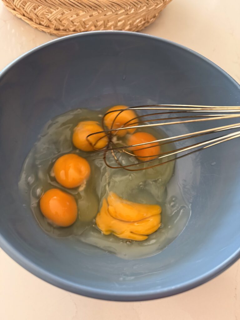 Whisking 6 eggs in a blue mixing bowl on the counter,