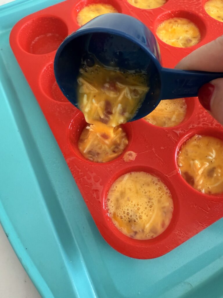 Pouring egg batter into red muffin pan in a light blue baking sheet on the counter.