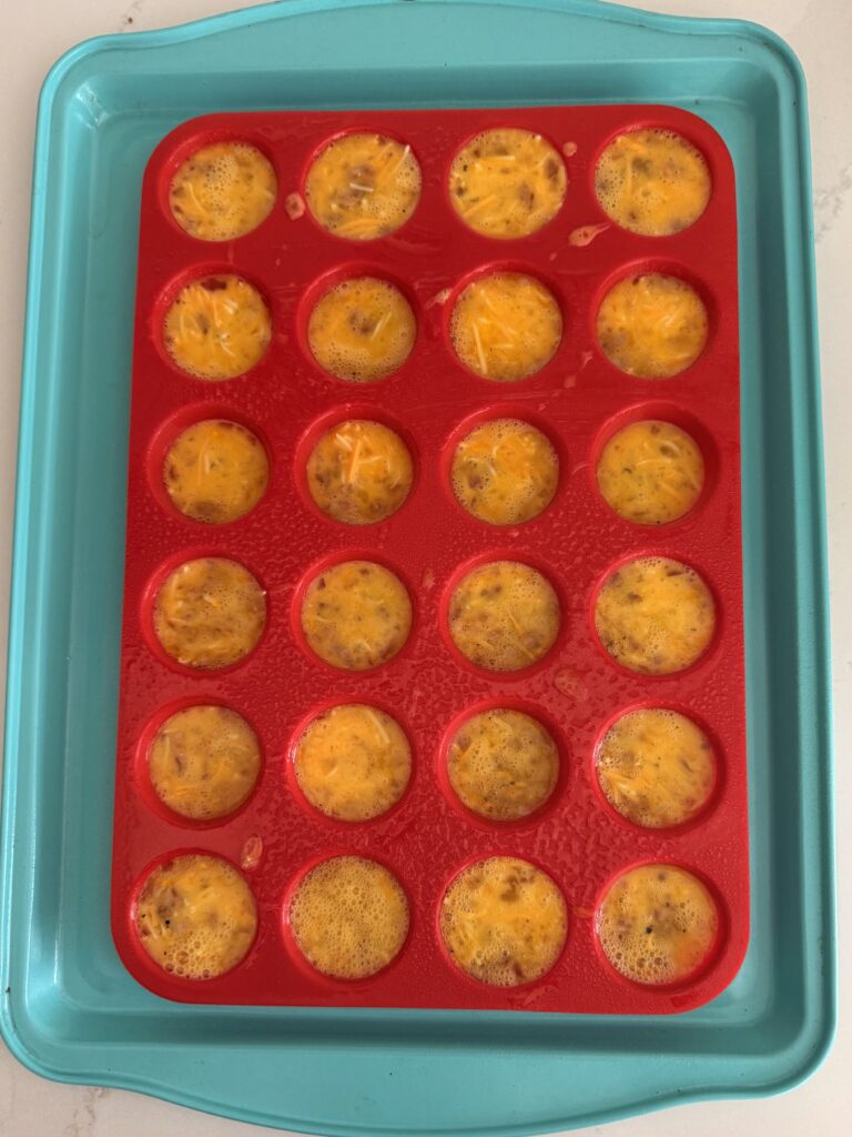 egg batter in red mini muffin pan on a light blue baking sheet on the counter.