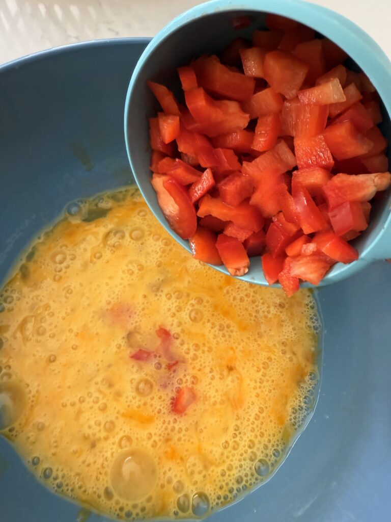 wicked eggs in a blender mixing bowl on the counter. finely chopped red pepper in a 1 cup measuring cup.