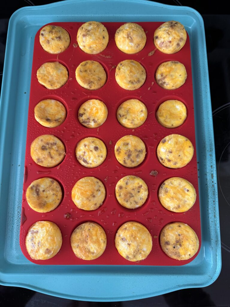 cooked mini egg bites in a red muffin pan on a light blue baking sheet on the oven top.