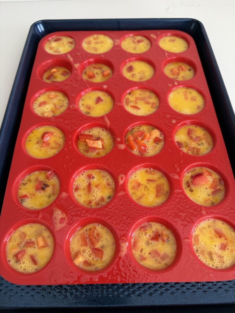 Filled mini muffin pan cups on a dark blue baking sheet on the counter.