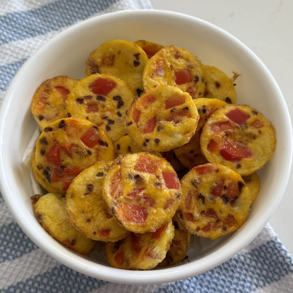 Spicy red pepper egg bites in a white bowl on a blue hand towel on the counter.