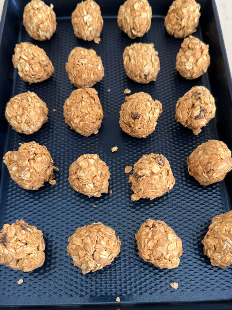 Rolled into balls are the no bake energy bites on a dark blue baking sheet on the counter.