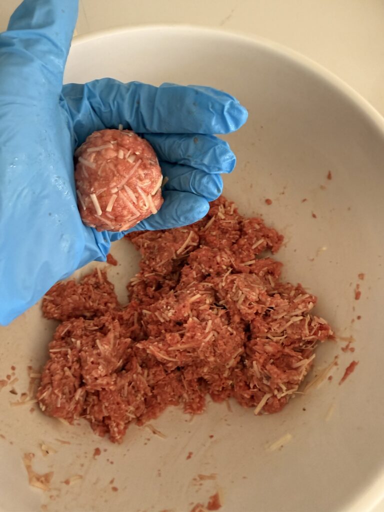 Using blue food prep gloves to form meatballs. Meat mixture in a large white mixing bowl on the counter.