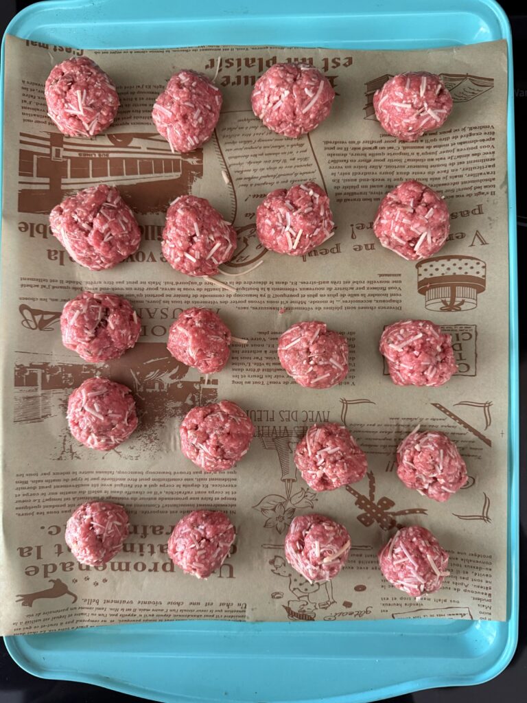 20 formed cheese and meat, meatballs on a line parchment paper blue baking sheet on the stove top.