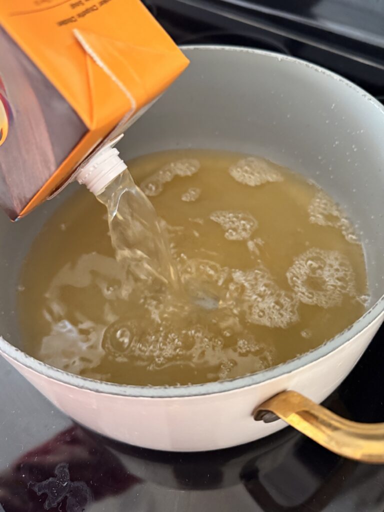 chicken broth being poured in a large pot on the stovetop.