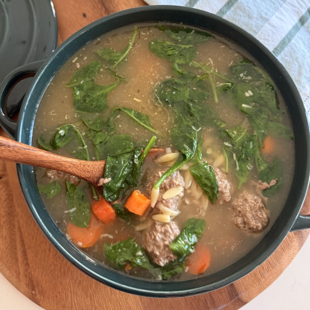 Italian Wedding Soup in a green pot on a brown cutting board on the counter.