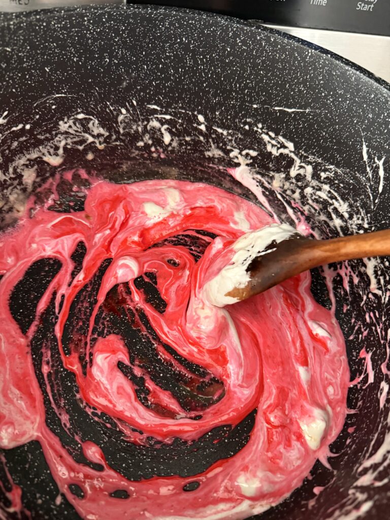 Pink food coloring melted marshmallows and butter are mixed in a large black pot on the stovetop.