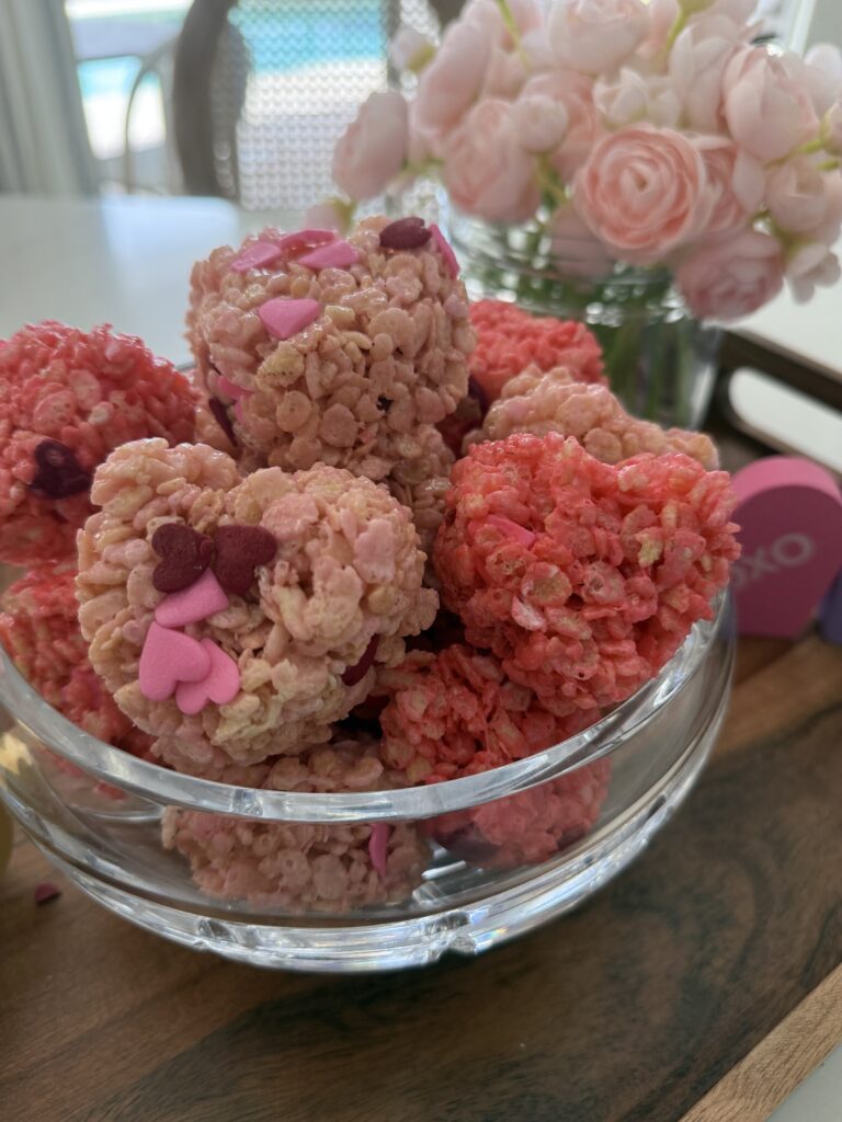 Valentine Rice Crispy hearts in a glass bowl on a brow tray with pink flowers in the background on the counter.