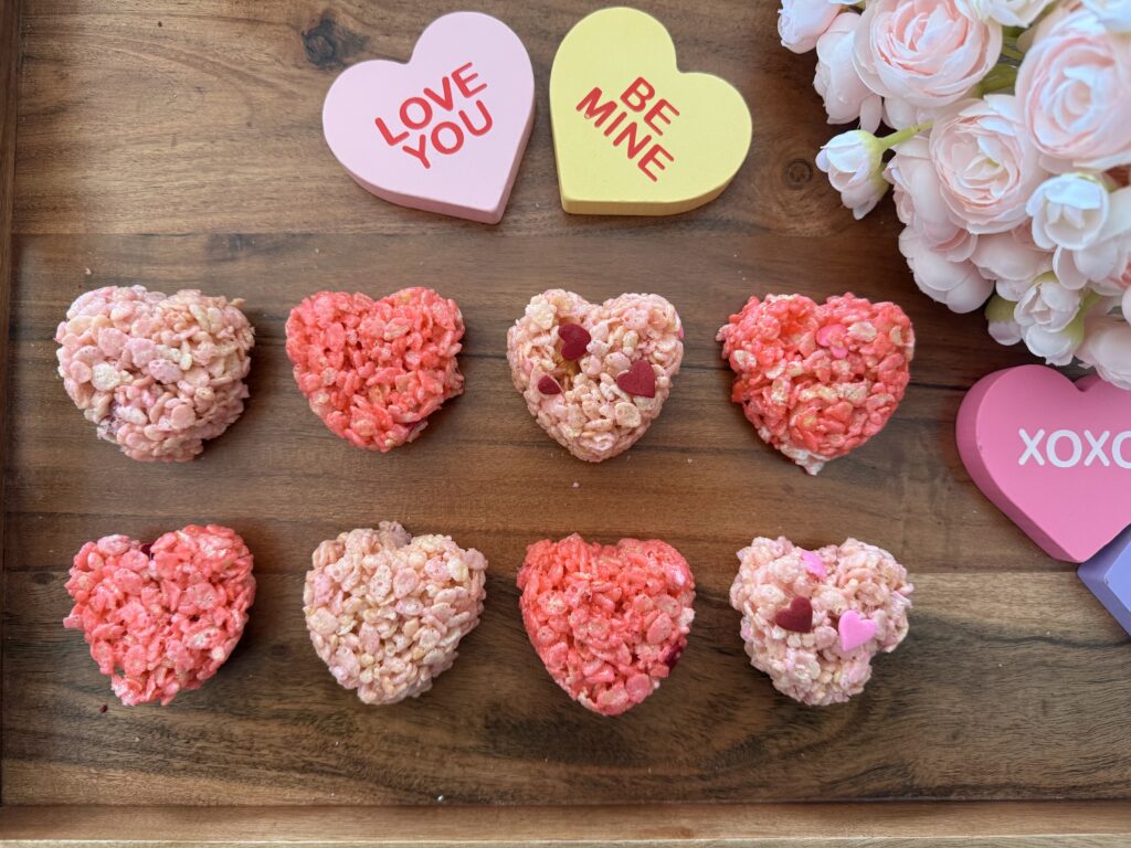 Valentine's Rice Crispy Treats on a brown tray with pink flowers and Valentine decorations on the counter.