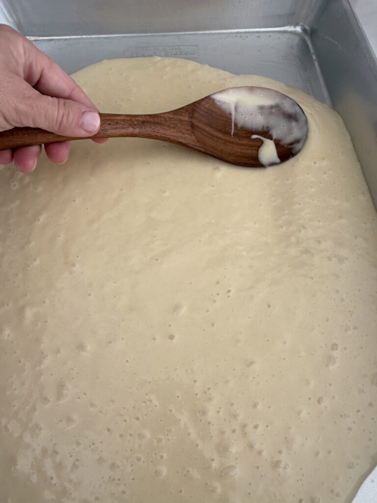 Using the back of a wooden spoon, and spreading the cake batter in an 18x13-inch rimmed cake pan on the counter.