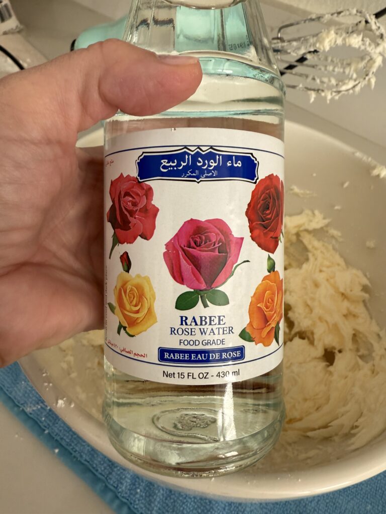 Holding a bottle of edible food-grade rose water on buttercream icing in a white bowl on the counter.