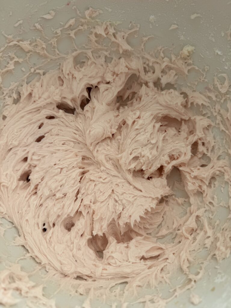 Blush buttercream icing in a large mixing bowl on the counter.