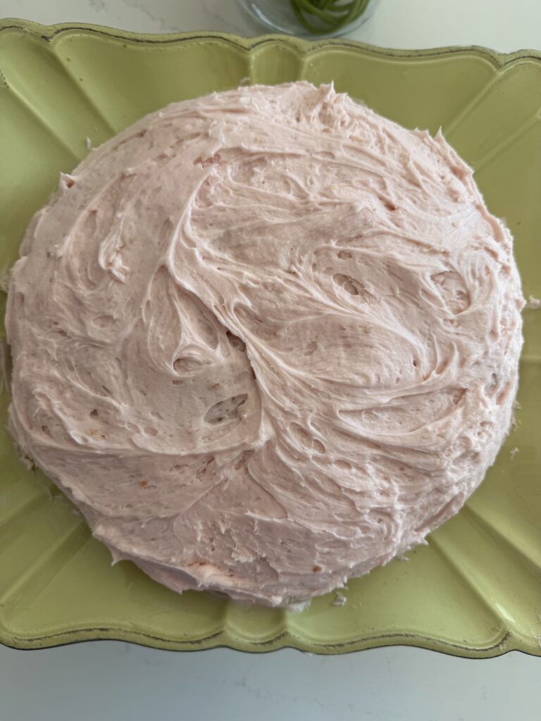 Iced blush buttercream vanilla cake on a light green cake stand on the counter.