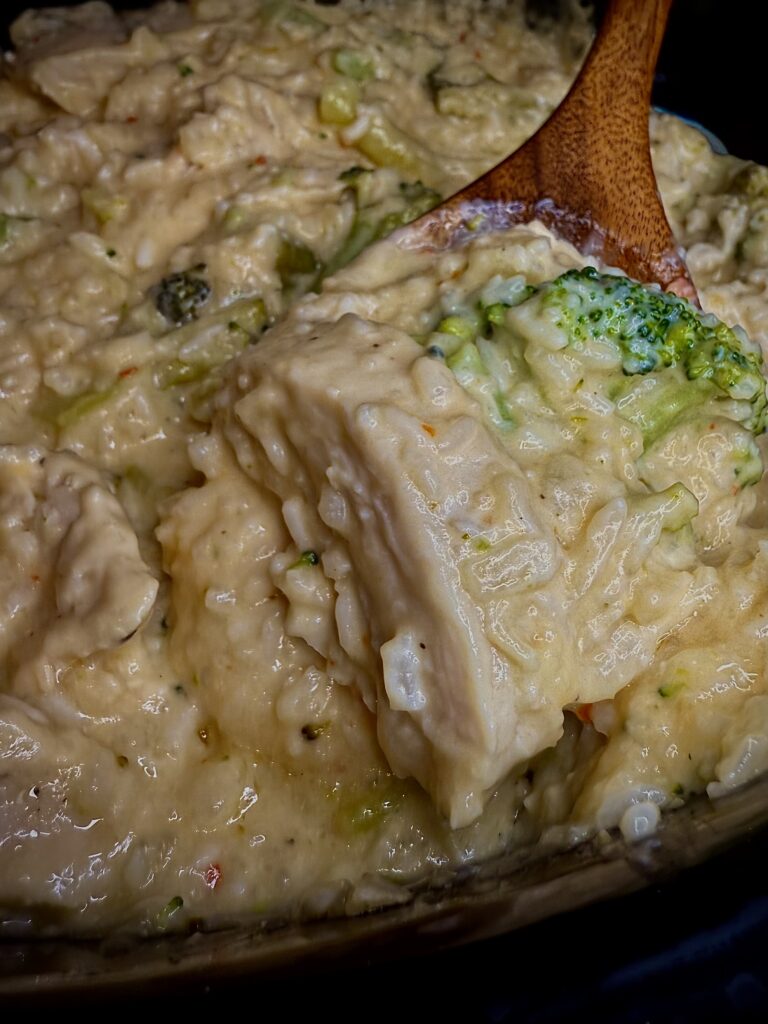 Slow cooker chicken, broccoli and rice casserole being stirred with a wooden spoon in the slow cooker on the counter.