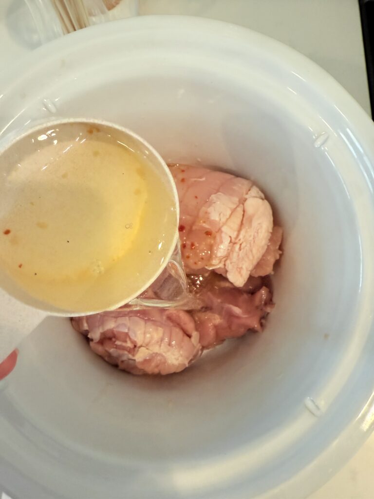 pouring white wine into the slow cooker over the turkey meat in the slow cooker.