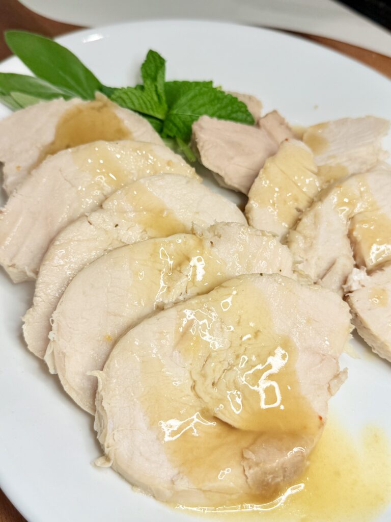 Slow cooker turkey with herbs covered in gravy on a white plate on the brown cutting board on the counter.