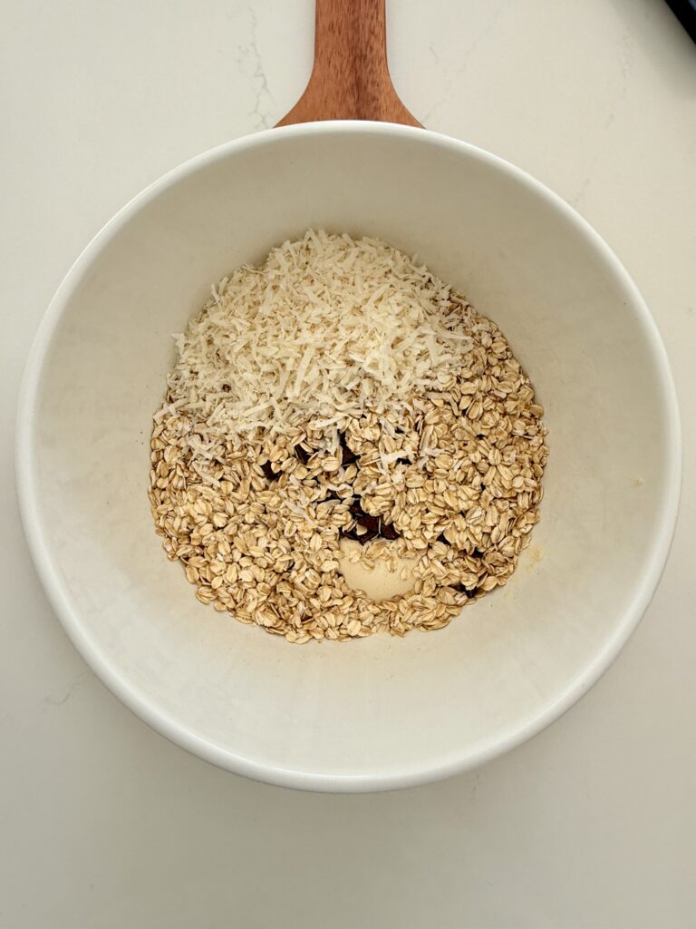 Rolled oats, vanilla protein powder, and semi-sweet chocolate chips in a large white mixing bowl on the counter.