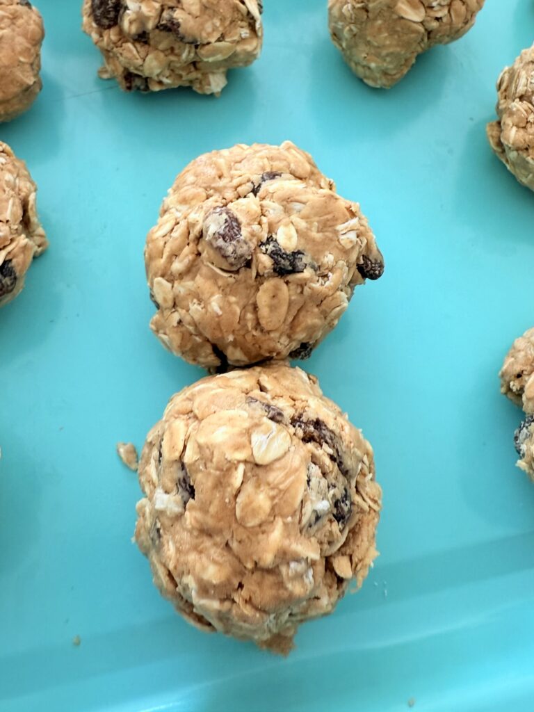 Balls of oatmeal raisin bites on a light blue baking sheet.