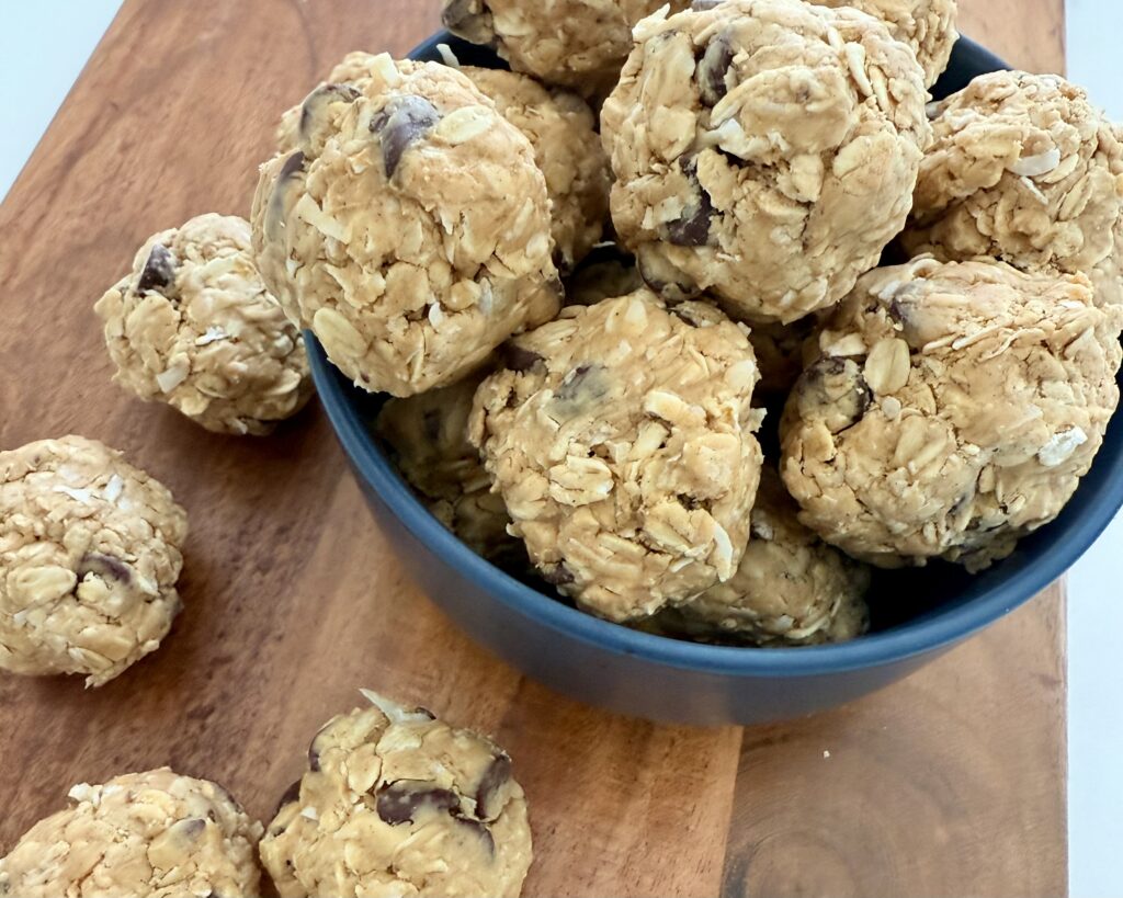 Choco-coconut snack bites in a dark blue bowl and on the brown cutting board on the counter.