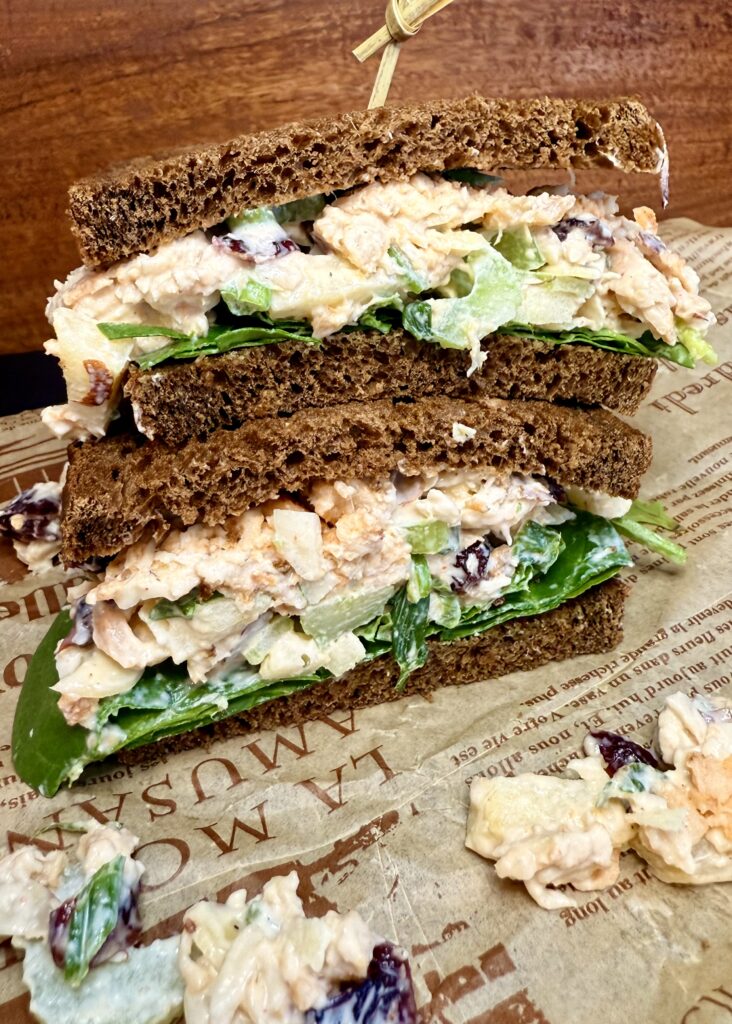 Chicken salad sandwich on parchment paper on a black cutting board on the counter.