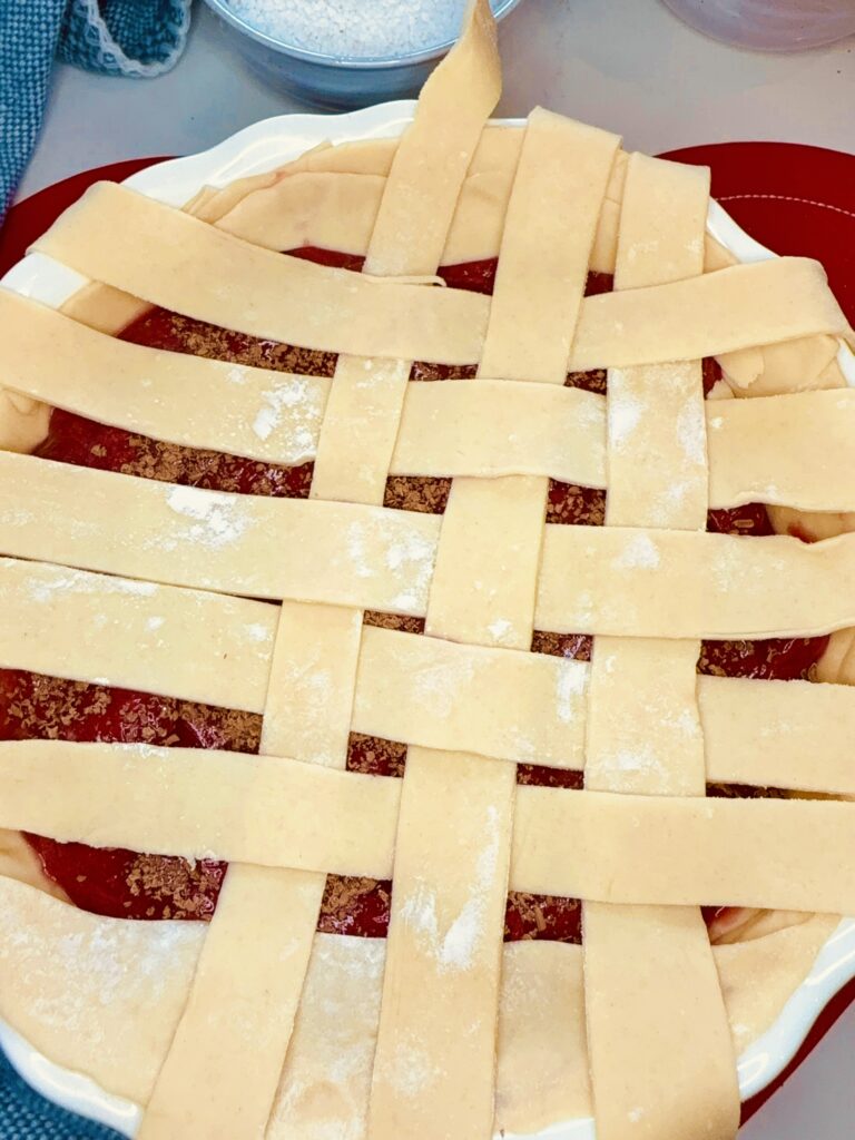 Weaved long pieces of raw pie crust, making a lattice pattern on top of the pie filling on the counter.