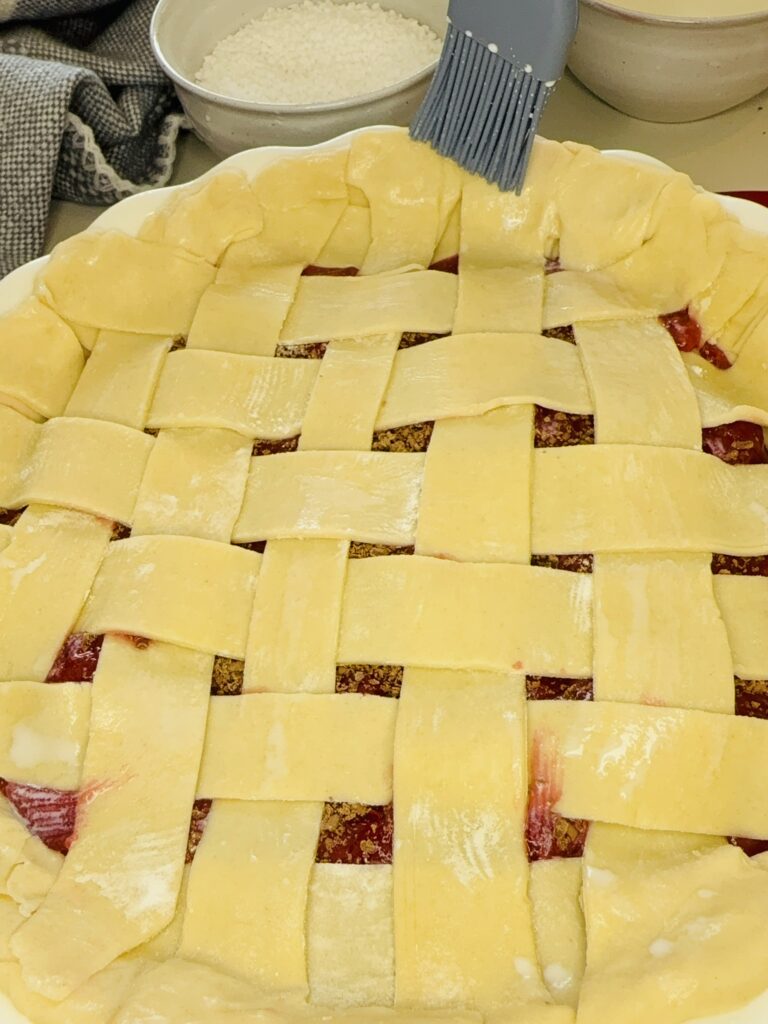 Weaved long pieces of raw pie crust, making a lattice pattern on top of the pie filling on the counter. 