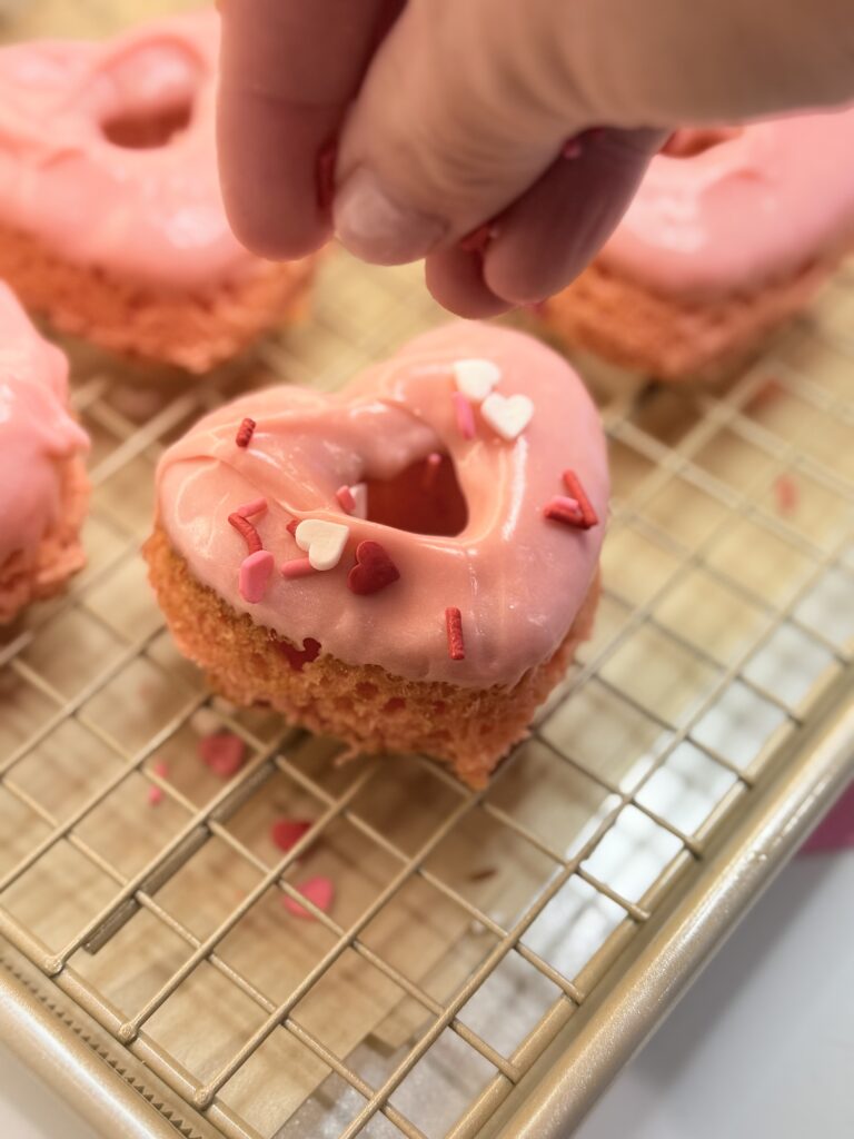 Love Struck cake donuts with sprinkles on a cooling rack on the counter.