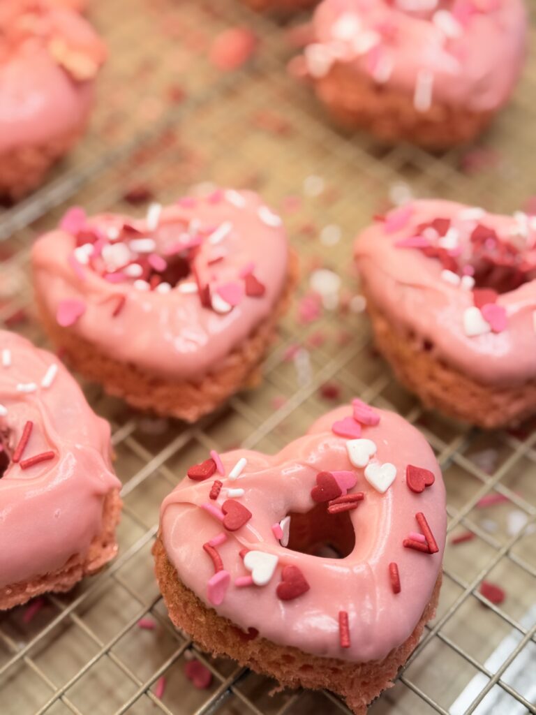 Love Struck cake donuts with sprinkles on a cooling rack on the counter.