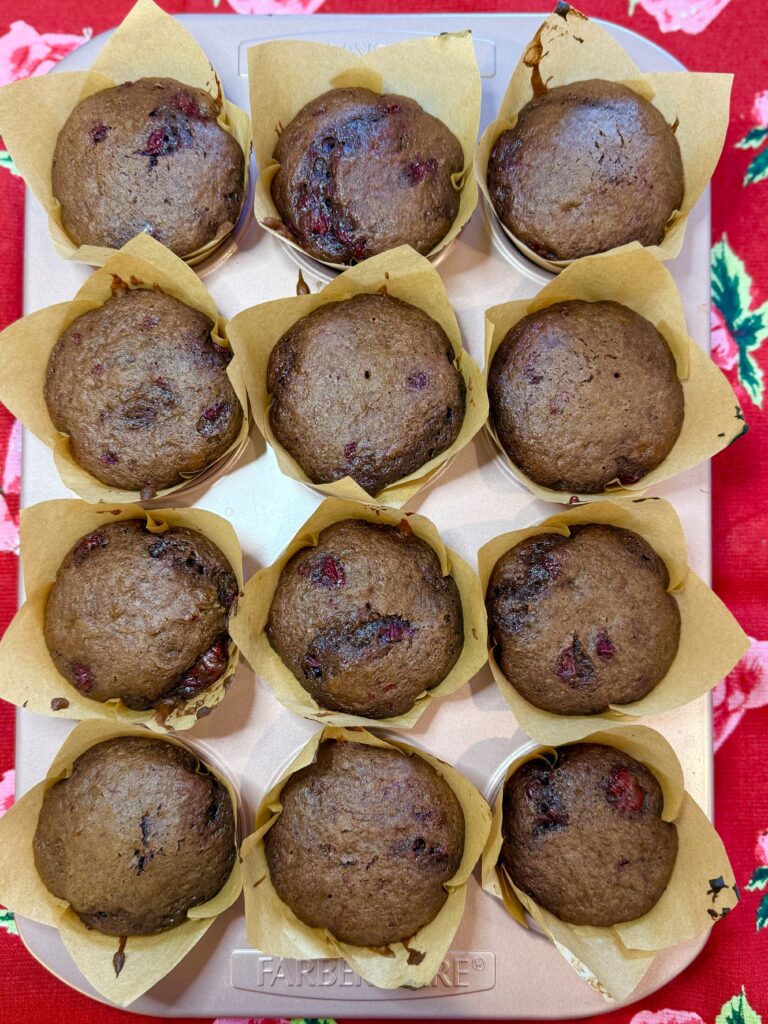 Cooled chocolate cherry muffins in a pink muffin tin on a red hand towel on the counter.