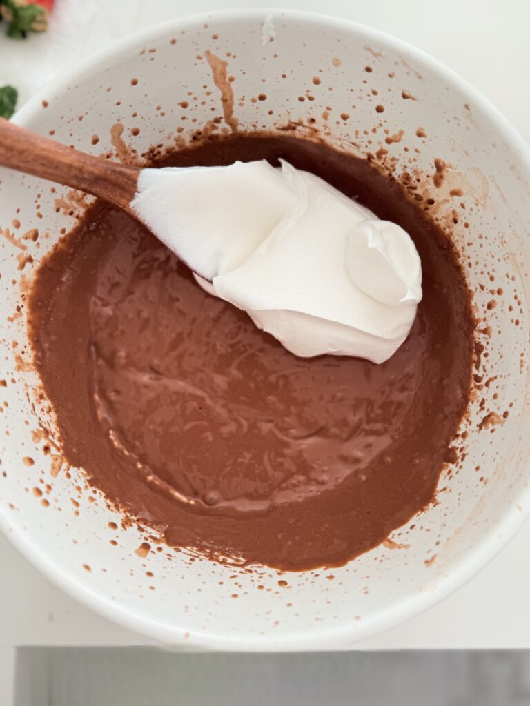 Cool Whip is poured into the chocolate instant pudding in a large mixing bowl on the counter.