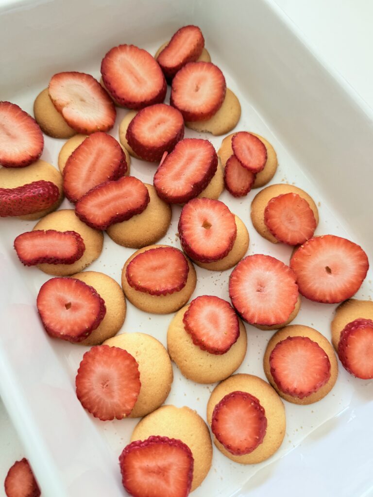 Sliced strawberries on top of vanilla wafers in a white baking dish on the counter.