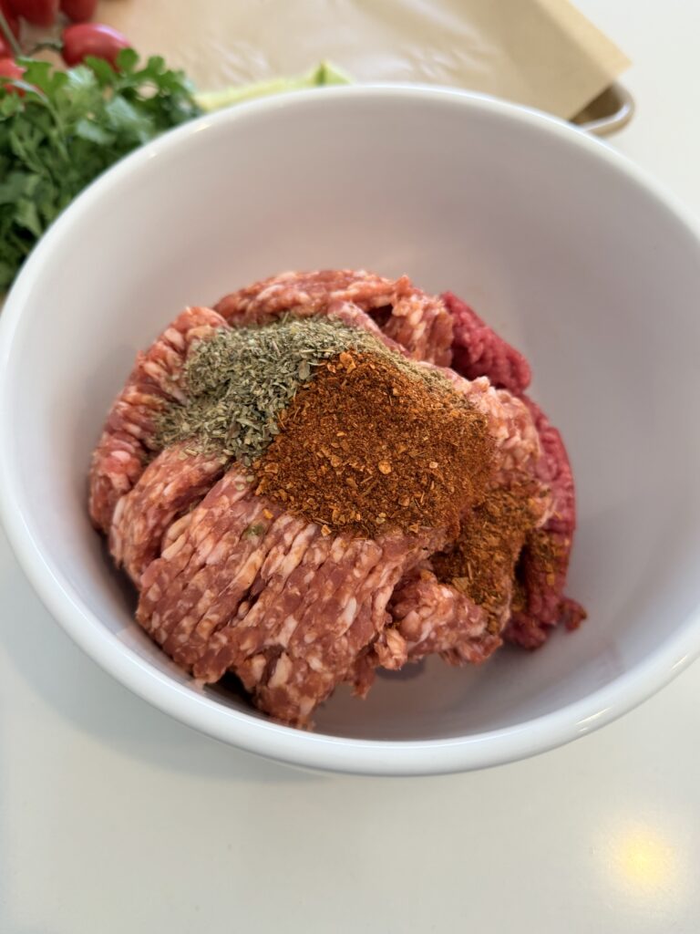 ground beef and spicy pork sausage with seasoning in a mixing bowl on the counter.