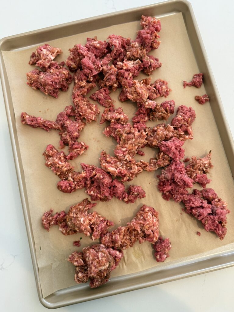 ground beef and spicy pork sausage with seasoning on a lined sheet pan on the counter.