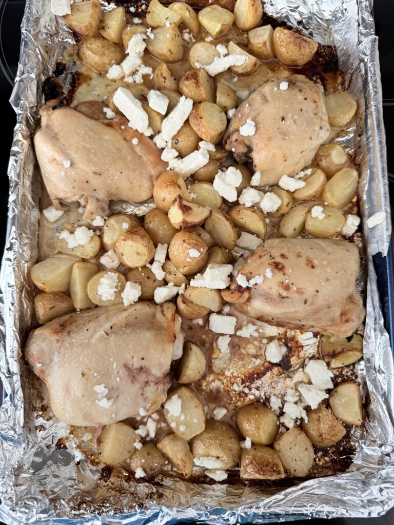 Baked Chicken thighs and halved-cut mini yellow Dutch potatoes with crumbled feta cheese on top on the stove top.