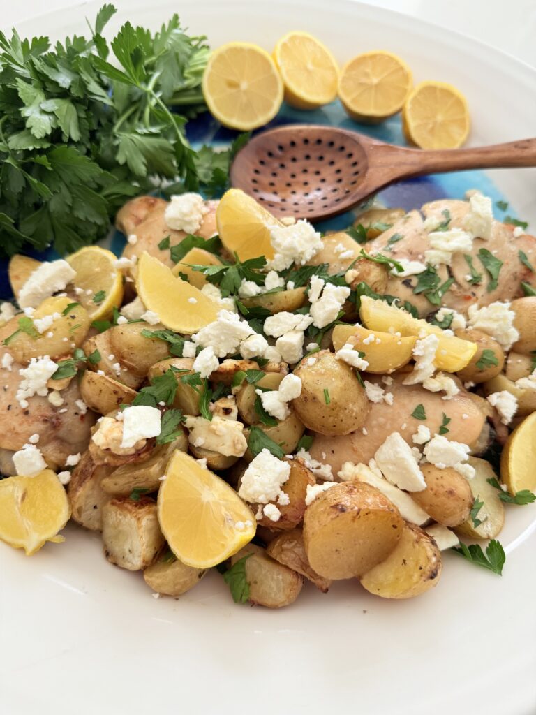 One pan greek chicken and potatoes on a blue and white platter surrounded by lemon halves and parsley.