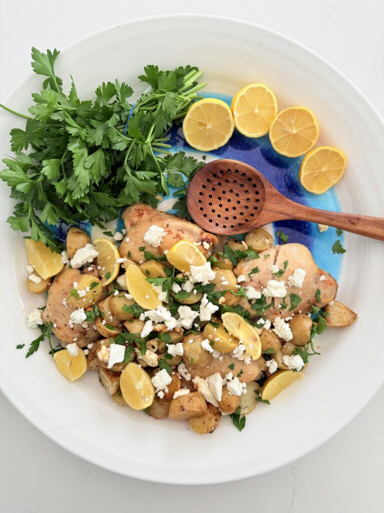 One pan greek chicken and potatoes on a blue and white platter surrounded by lemon halves and parsley.