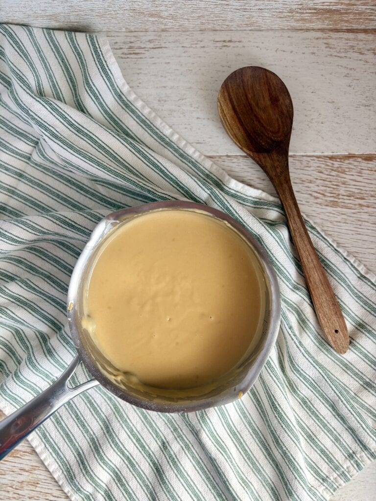 beer cheese dip in a saucepan next to a wooden spoon on a striped towel.