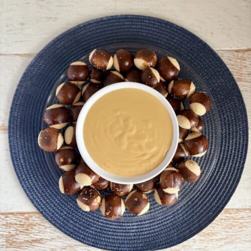 Beer Cheese Dip in a white bowl surrounded by pretzel bites on a plate.