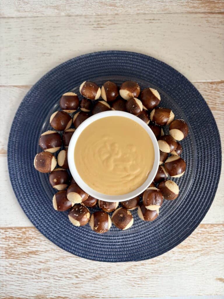 Beer Cheese Dip in a white bowl surrounded by pretzel bites on a plate.
